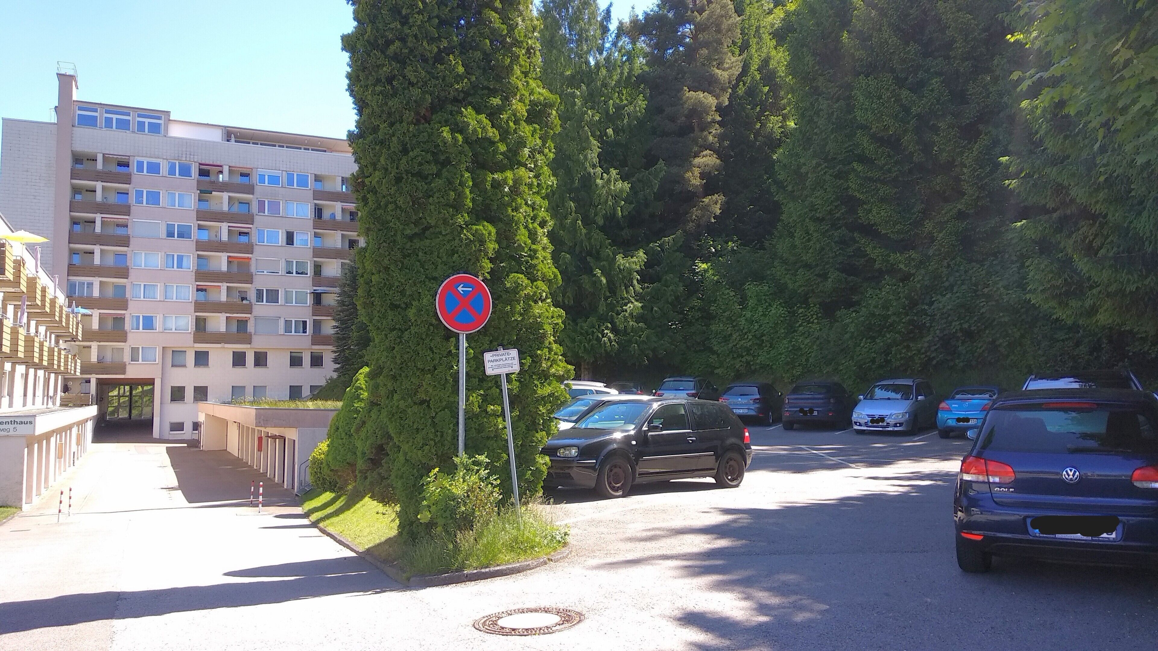 A parking area with a no-parking sign, a private parking sign, and a row of parked cars.