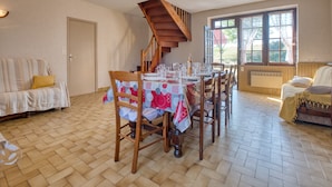 Un comedor con una escalera de madera, una mesa de comedor con sillas y un ventanal con cortinas.