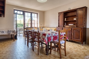 A dining area with a table set for four, wooden chairs, a cabinet, and a view through a window. - La Coccinelle – Spacious and Family-Friendly Holiday Home in the Heart of the Périgord Noir (Saint-Geniès)