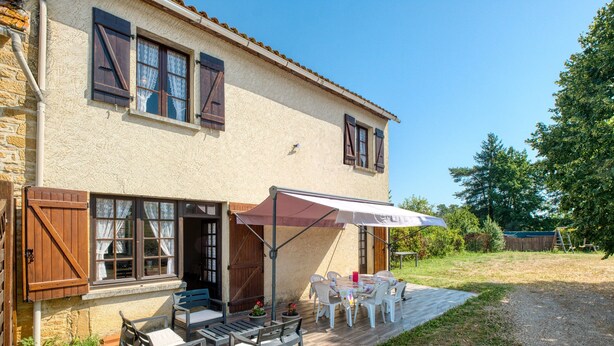 Una casa de dos pisos con un patio que cuenta con mobiliario exterior y una zona de estar cubierta.