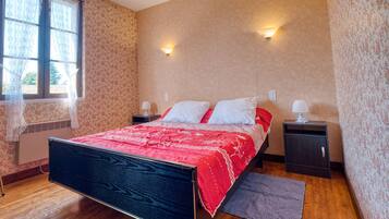 A bedroom with a bed, nightstands, a window with curtains, and a wall-mounted light fixture.