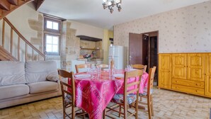 Un comedor con una mesa dispuesta para cuatro, un sofá, una escalera y una cocina al fondo.
