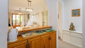 Una cocina con armarios de madera, encimera blanca, hervidor y un reloj enmarcado.