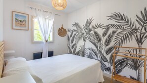 Ein Schlafzimmer mit einem Bett, einer Hängelampe, einem Fenster mit Vorhängen, einem Wandgemälde und einem Holzregal.