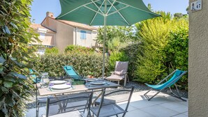 Eine Terrasse im Freien mit Esstisch, einem grünen Sonnenschirm und zwei Liegestühlen.