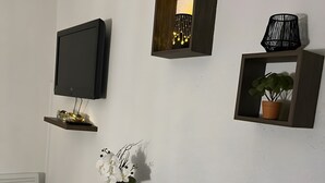 Une pièce avec un téléviseur fixé au mur, une petite table sur laquelle est posée une plante en pot et un objet décoratif accroché au mur.