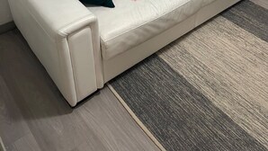 Un canapé en cuir blanc agrémenté de deux coussins vert foncé, un tapis à motifs et un tableau accroché au mur.