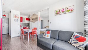 Ein modernes Wohnzimmer mit einem grauen Sofa, roten Sesseln, einem Esstisch und einer Küche im Hintergrund.