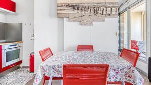 Ein Essbereich mit Tisch und Stühlen, eine Küche mit Backofen und ein an der Wand befestigtes Kunstwerk.