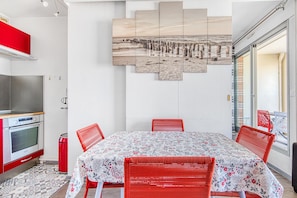 Un comedor con mesa y sillas, una cocina con horno, y una obra de arte colgada en la pared.