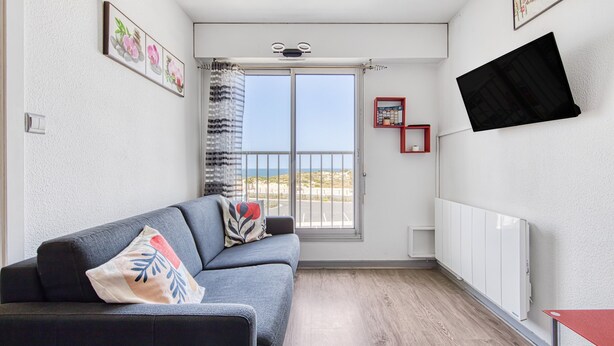 Ein modernes Wohnzimmer mit grauem Sofa, einem Fenster mit Blick, einem Wand-Fernseher und einer Heizung.