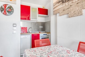 A compact kitchen with red cabinets, a sink, and a dishwasher.