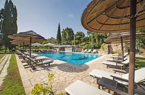 A swimming pool with lounge chairs and umbrellas, surrounded by stone tiles and greenery.