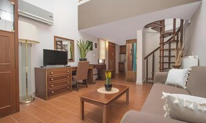 A living room with a TV, wooden furniture, a staircase, and a plant.