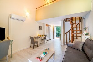 A modern living room with a sofa, a coffee table, and a TV. There is a staircase with a wooden railing leading to another room.