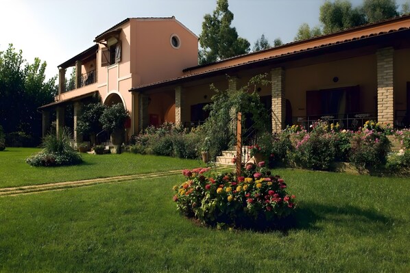 Un edificio a due piani con un balcone, un giardino fiorito e un cielo sereno.