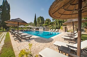 Una piscina con lettini e ombrelloni, circondata da piastrelle in pietra e vegetazione.