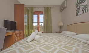 Une chambre dâhĂŽtel comprenant un lit, un bureau avec une tĂ©lĂ©vision, une fenĂȘtre avec des rideaux, un climatiseur fixĂ© au mur et un tableau.