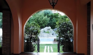 An arched entrance leading to a garden with a rock feature and a fountain.