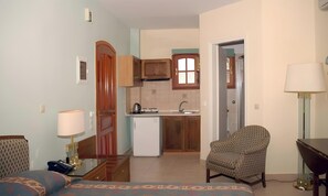 Habitación de hotel compacta con cama, escritorio, silla, kitchenette pequeña y baño.