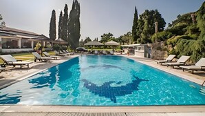 A swimming pool with lounge chairs, a gazebo, and tall trees.