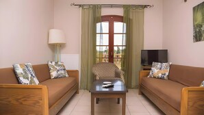 Un salon avec deux canapés, une table basse, une lampe, un téléviseur et une fenêtre avec des rideaux.