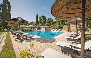 A swimming pool with lounge chairs and umbrellas, surrounded by stone paving and greenery.