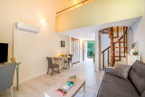 A modern living room with a sofa, a coffee table, and a TV. There is a staircase with a wooden railing leading to another room.