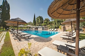 A swimming pool with lounge chairs and umbrellas, surrounded by stone tiles and greenery.