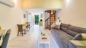 Een moderne woonkamer met een bank, een salontafel, een eethoek met stoelen, een trap en uitzicht op de omgeving.