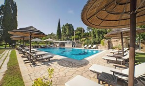 Une piscine entourée de chaises longues et de parasols, le tout bordé de dalles de pierre et de verdure.