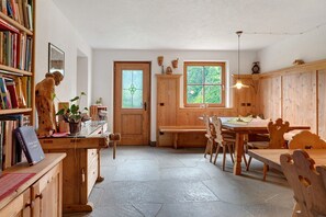A wooden interior with a dining table, chairs, a bookshelf, and a door with a window.