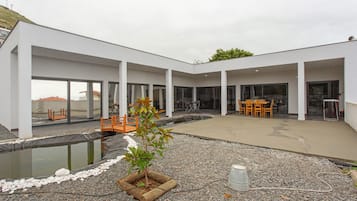 A modern building with a covered outdoor area, a small pond, and outdoor furniture.