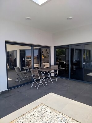 A modern outdoor patio with a glass enclosure, metal-framed chairs, and a table.