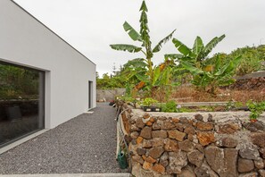 A modern building with a stone retaining wall, a banana plant, and a gravel pathway. - Studio 'Mariana' with Atlantic View, Culinary Experience and Unique Hospitality (Gaula)