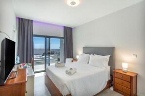 A hotel room with a bed, bedside tables, a TV, and a view of the outdoors.