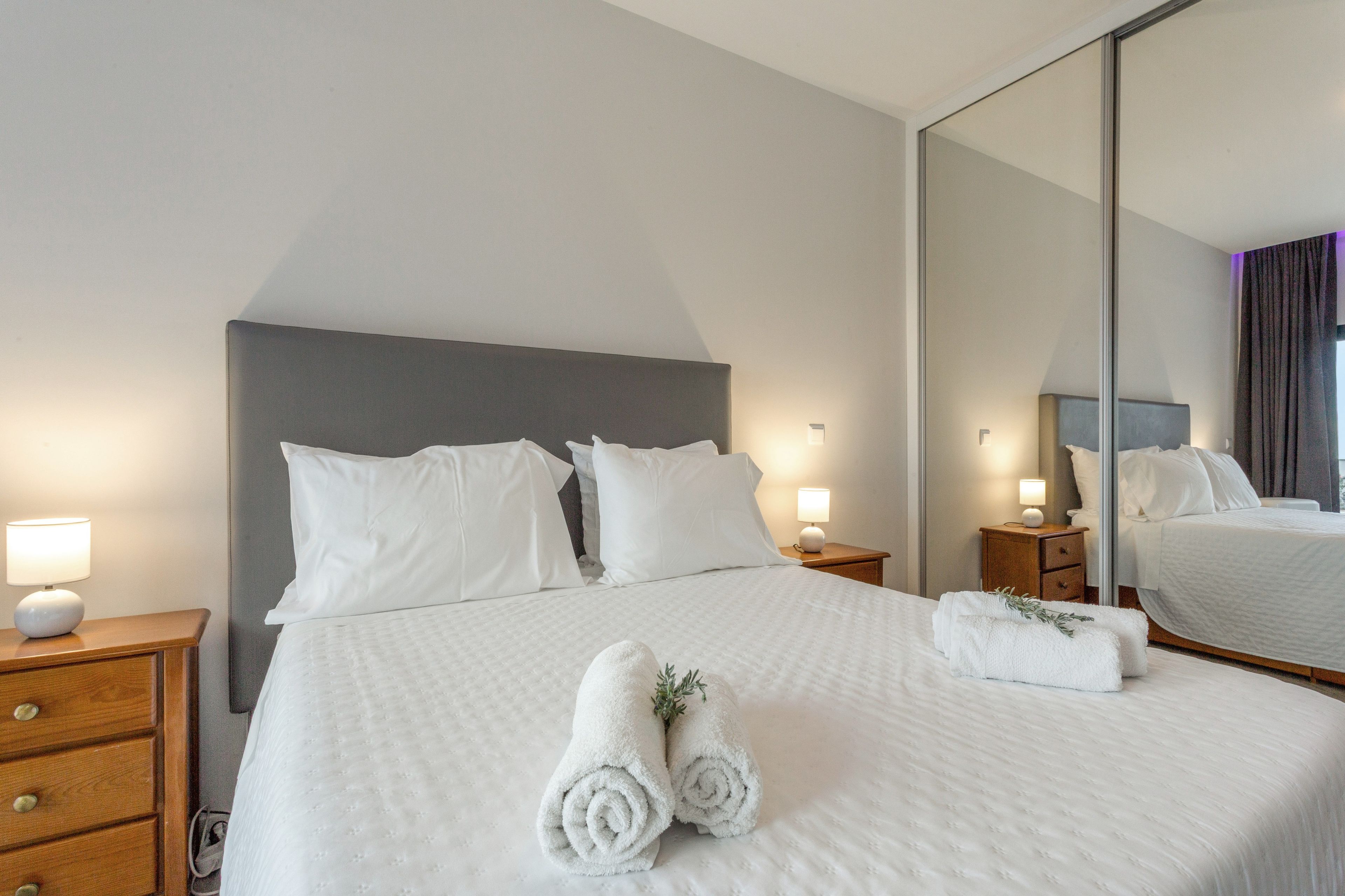 A hotel room with a large bed, two bedside tables, a nightstand, a mirror, and a dresser.