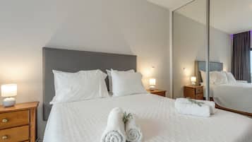 A hotel room with a large bed, two bedside tables, a nightstand, a mirror, and a dresser.