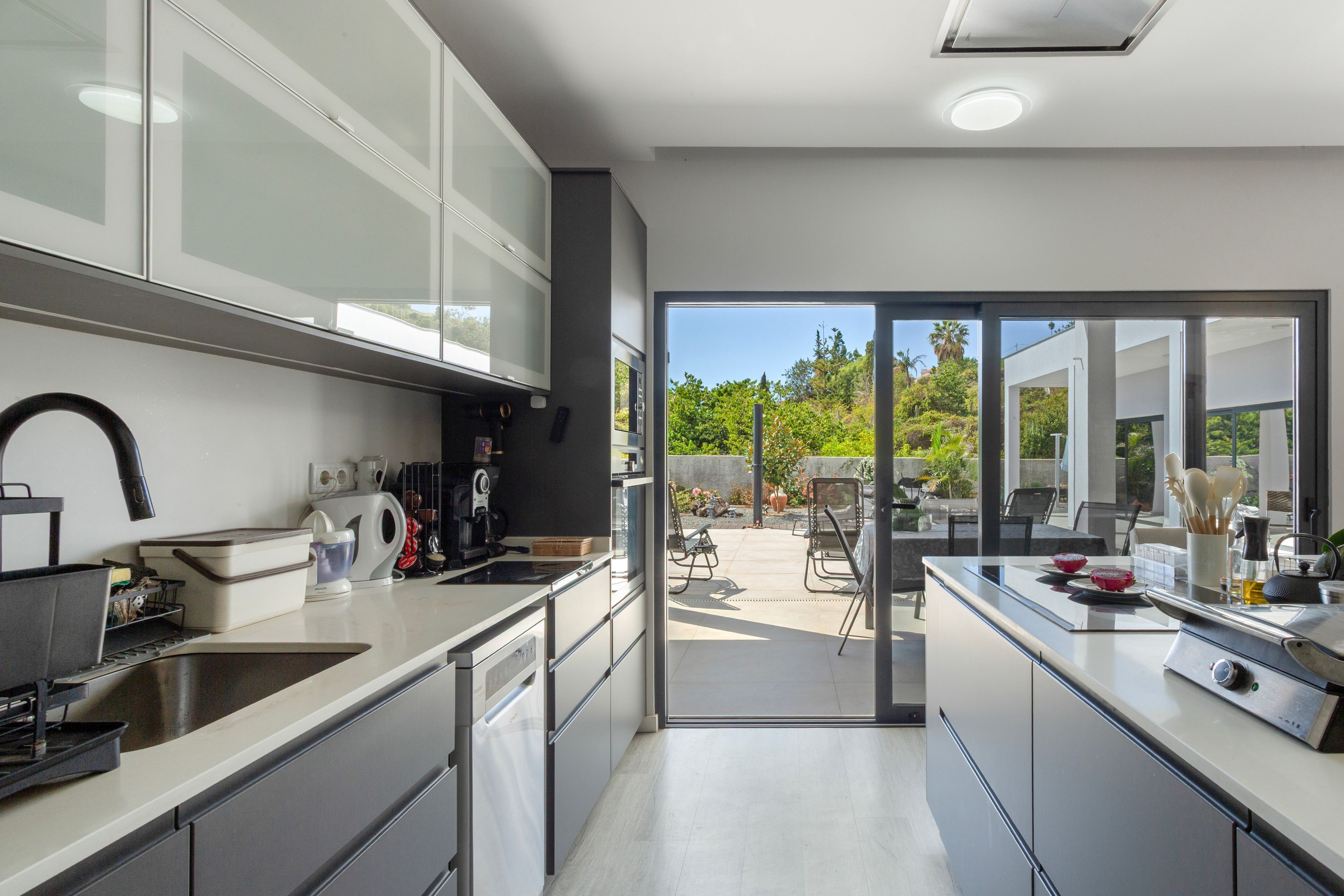 A modern kitchen with integrated appliances, a dining area with outdoor seating, and a view of a garden.