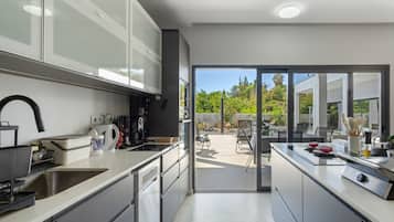 A modern kitchen with integrated appliances, a dining area with outdoor seating, and a view of a garden.