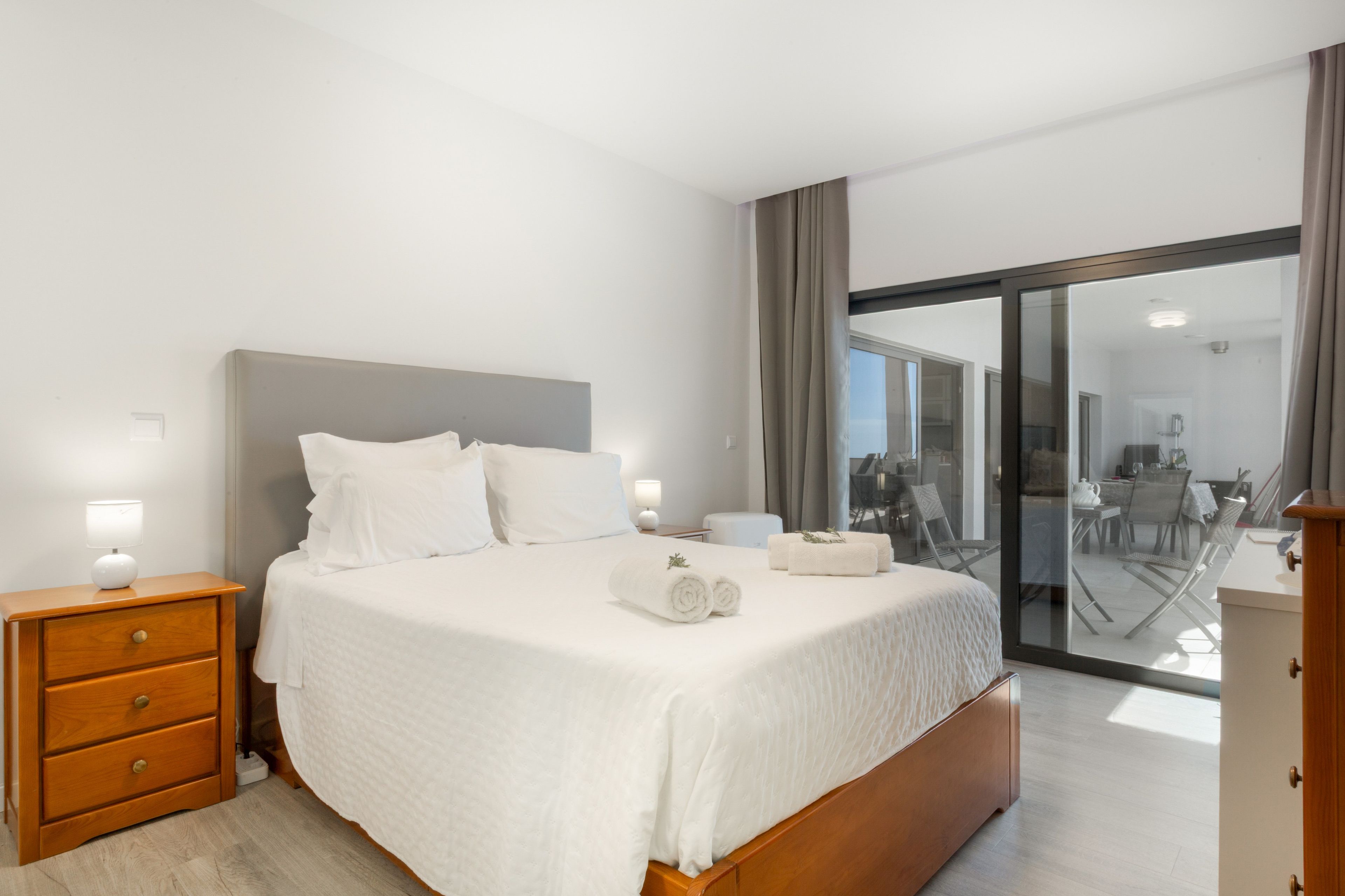 A modern hotel room with a large bed, a wooden nightstand, a desk, and a view of the outdoor area.