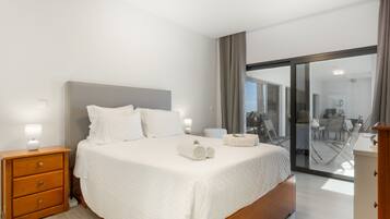 A modern hotel room with a large bed, a wooden nightstand, a desk, and a view of the outdoor area.