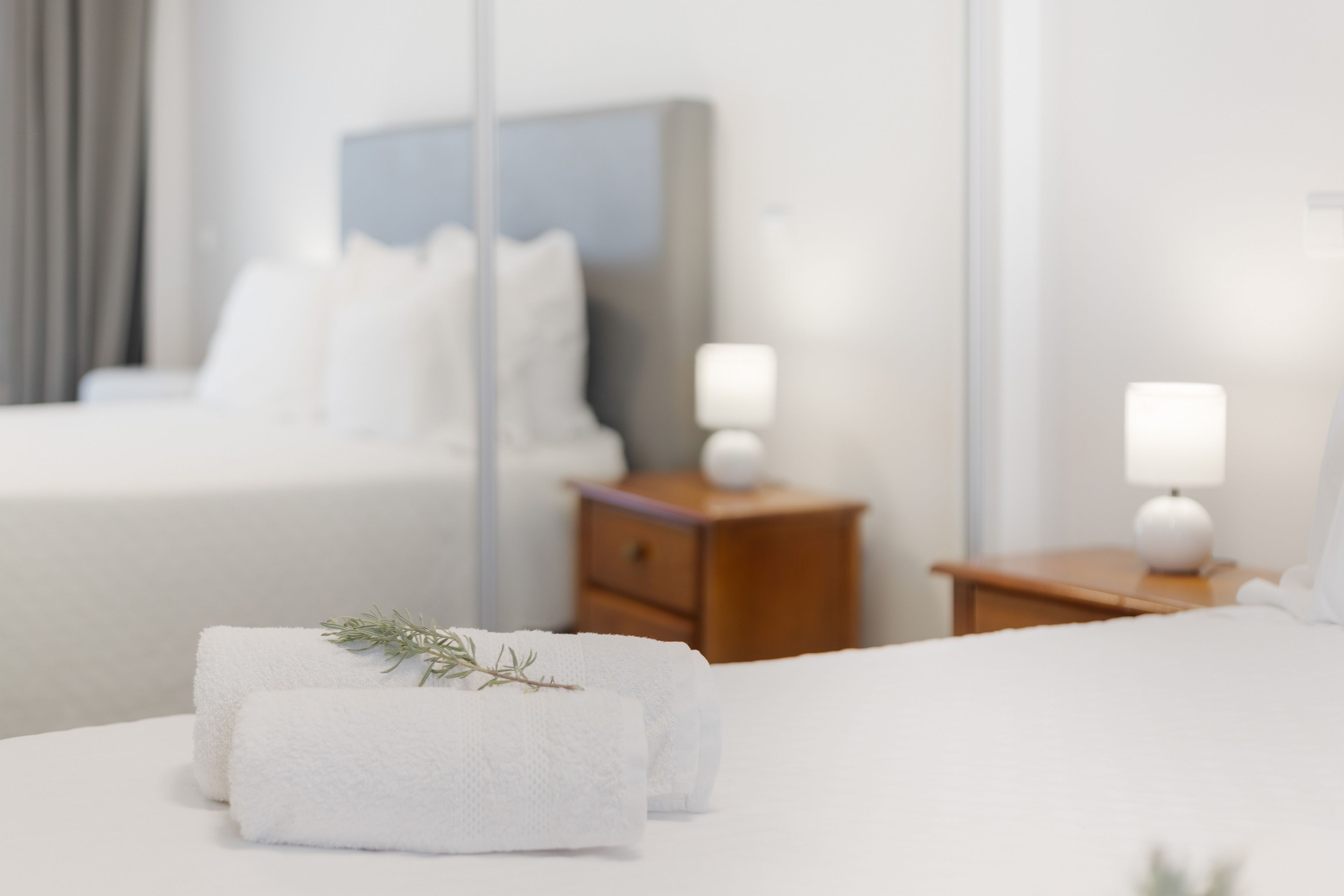 A neatly made bed with white linens and a folded towel with a sprig of greenery.