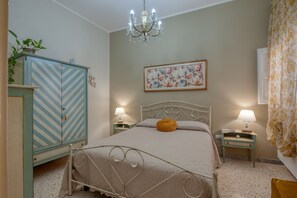 Een slaapkamer met een bed, een dressoir, een kroonluchter, een schilderij en twee nachtkastjes met lampen.