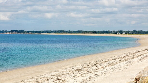 A beach with clear water, a sandy shore, and a distant shoreline with buildings.