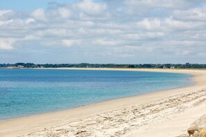 Une plage à l’eau claire, avec un rivage sablonneux et une ligne d’horizon lointaine où l’on aperçoit des bâtiments.