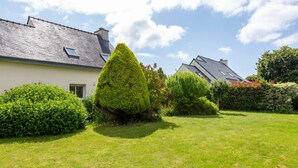 A residential property with a well-maintained lawn, a conical hedge, and a house with a sloped roof.