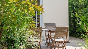 A patio with a table and chairs, surrounded by greenery.