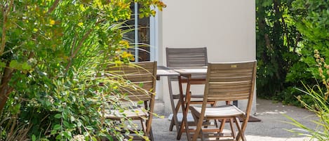 A patio with a table and chairs, surrounded by greenery.