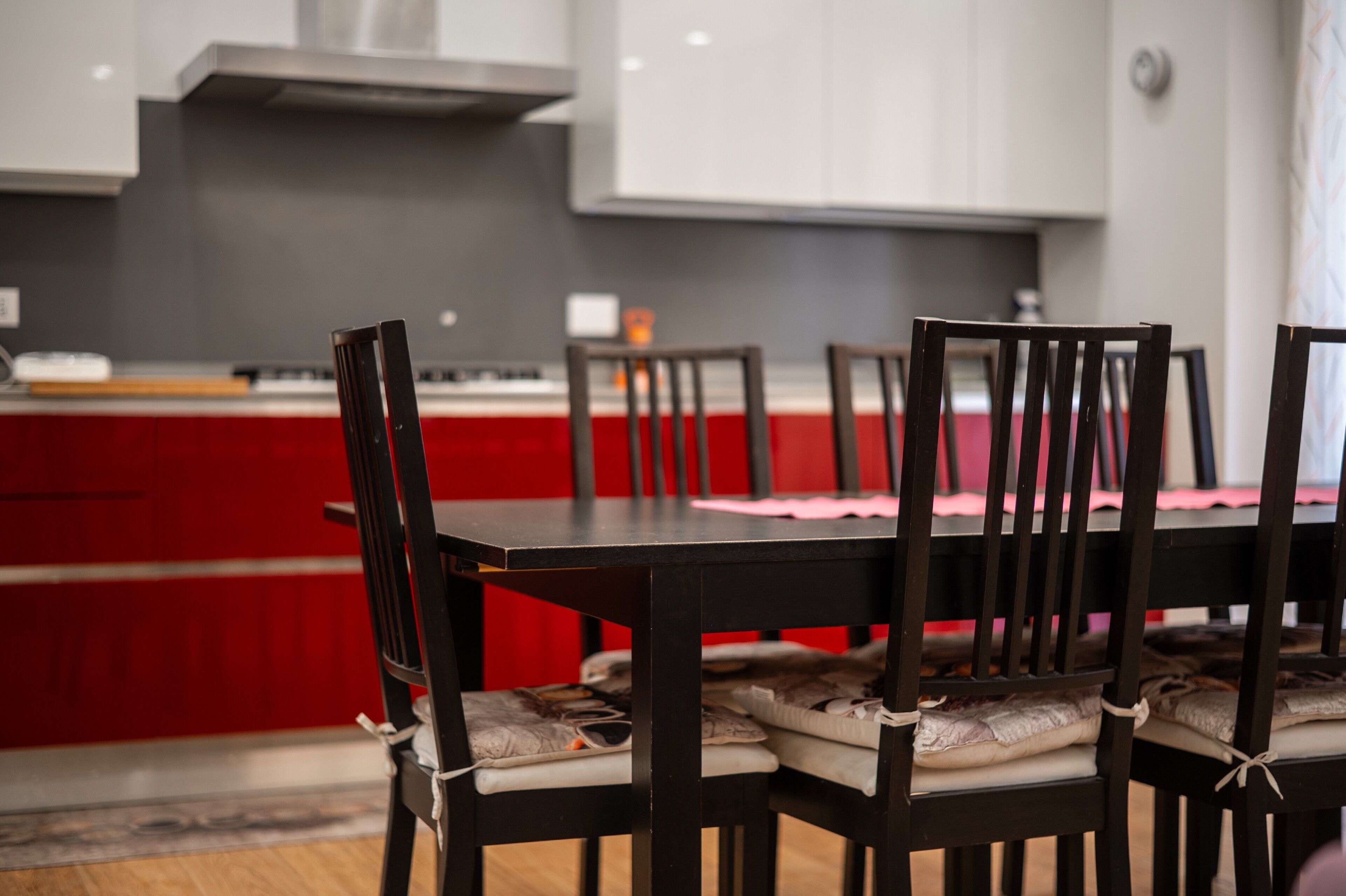 Un coin repas agrémenté d’un mur d’accent rouge, une cuisine en arrière-plan et une table dressée pour quatre personnes.